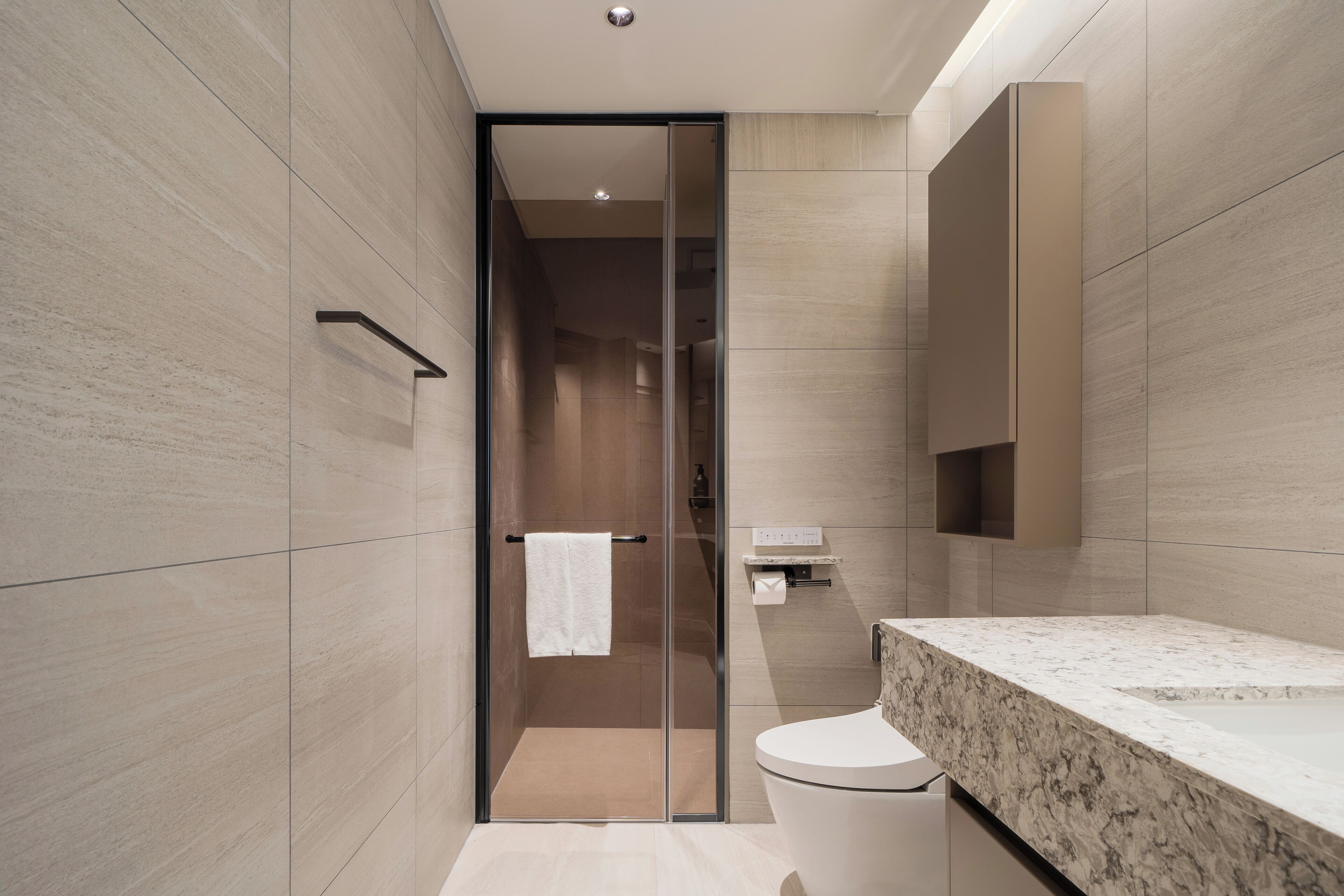 A modern bathroom with a glass shower enclosure, a marble countertop, and a large mirror.