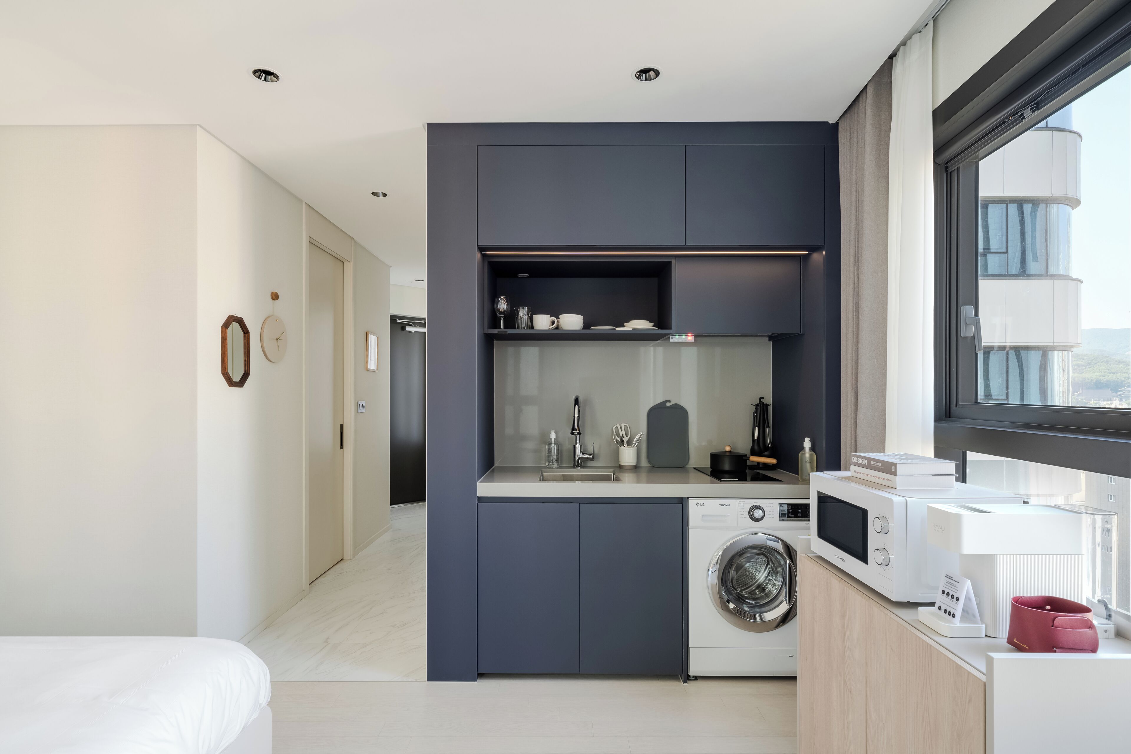 A compact kitchen with a washing machine, microwave, and a small countertop area.