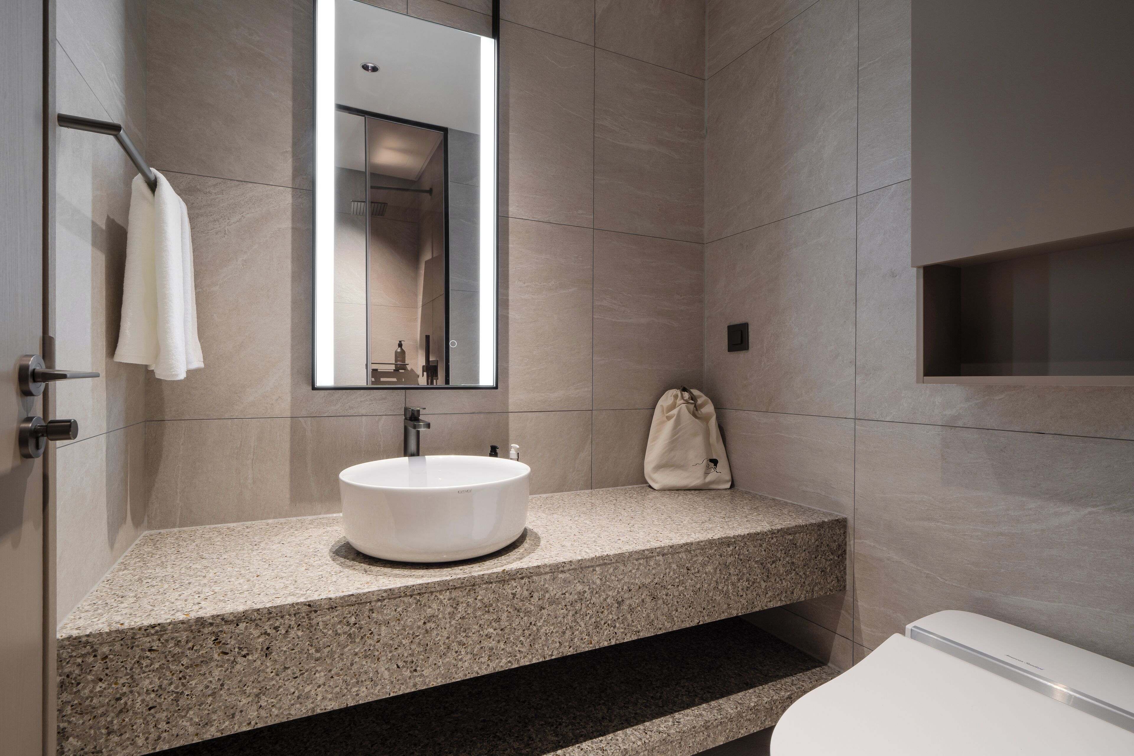 Un baño moderno con encimera de granito, un lavabo redondo, un espejo y un inodoro.