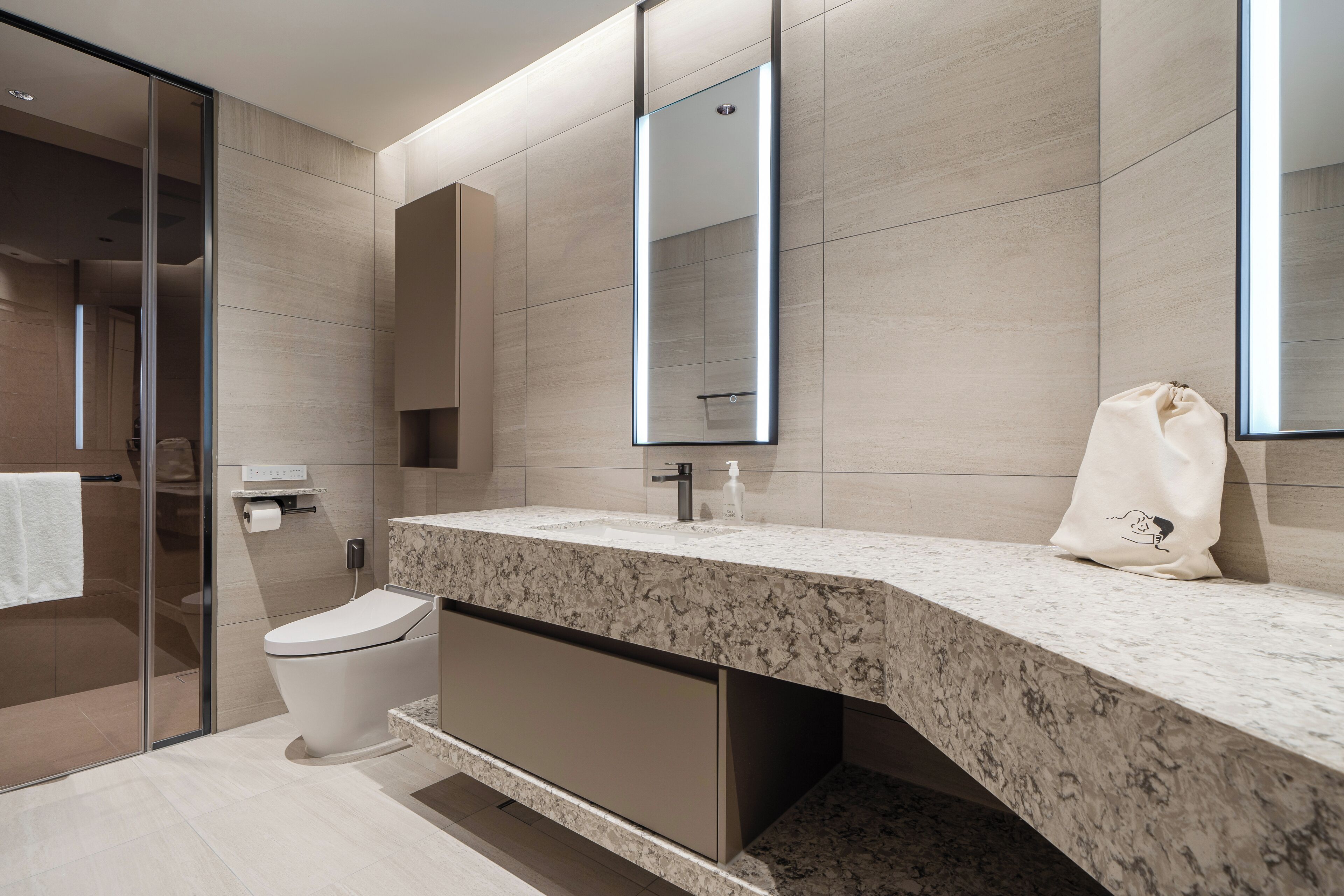 Un baño moderno con encimera de mármol, inodoro, cabina de ducha con mampara de cristal y un espejo grande.