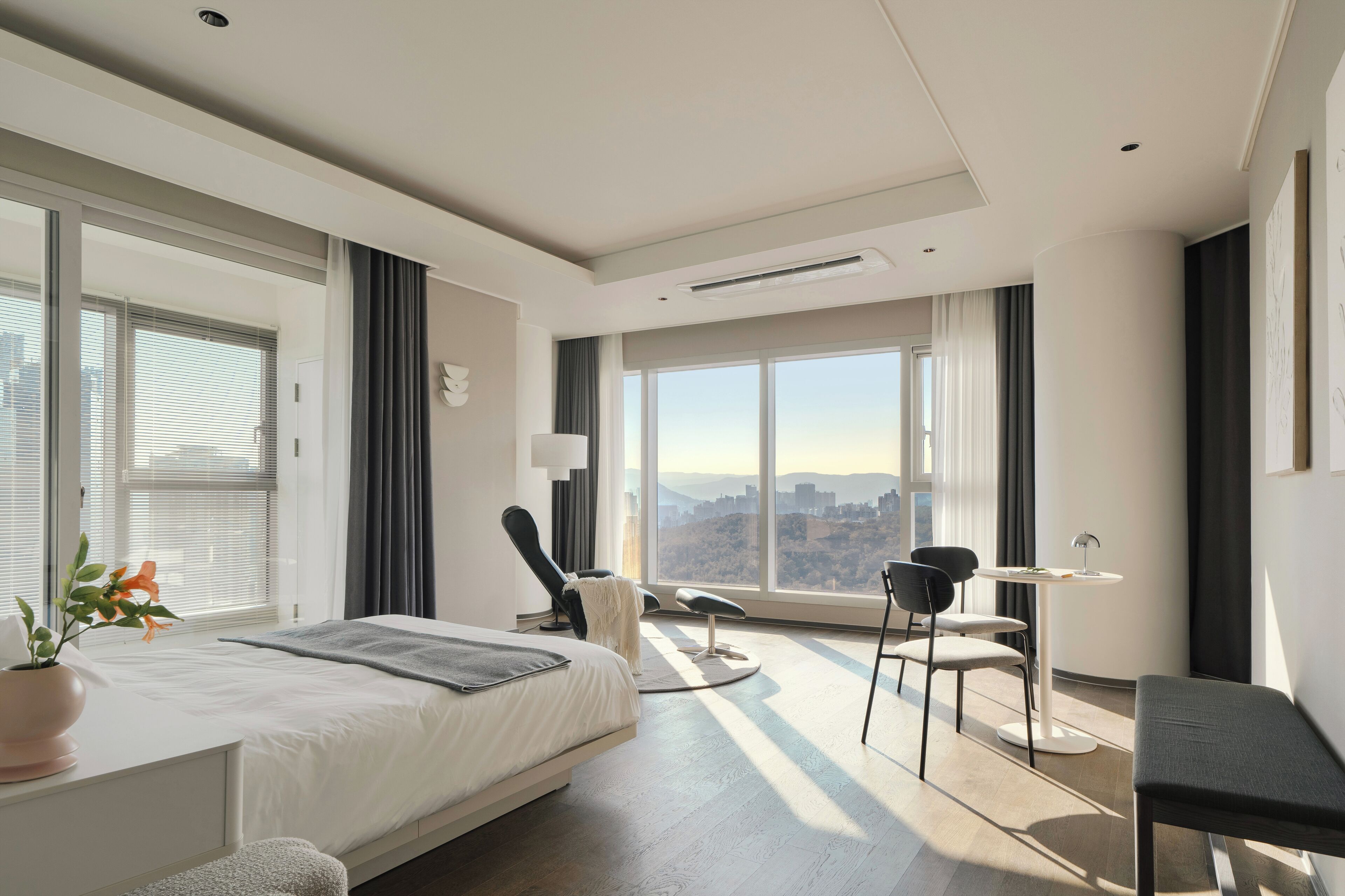 A modern hotel room with a large bed, a desk, a chair, and a view of the city.