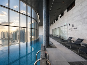 A modern indoor pool with a city view, lounge chairs, and a Paragraf sign.