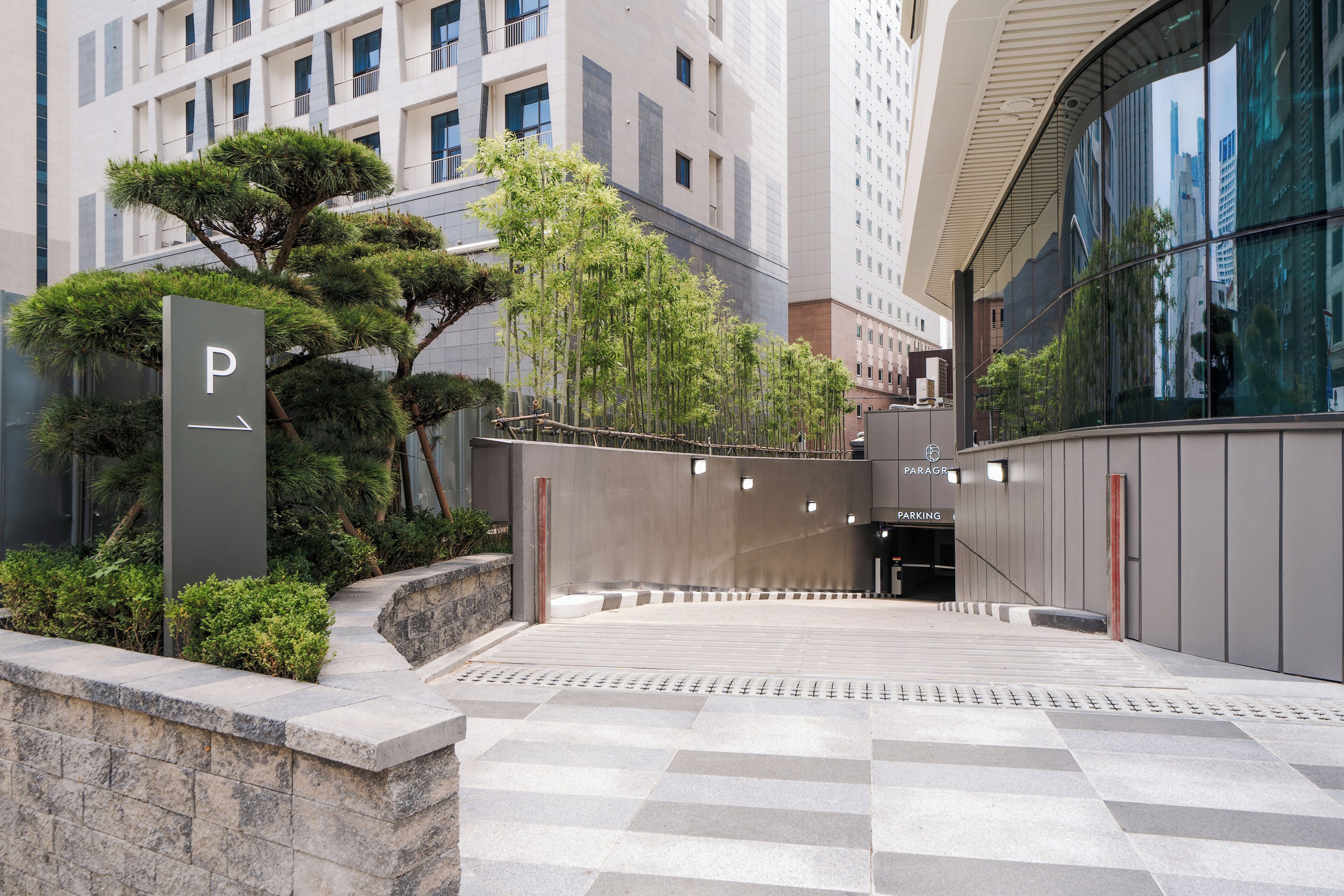 A modern building entrance with a parking sign, a staircase, and a glass facade reflecting the city.
