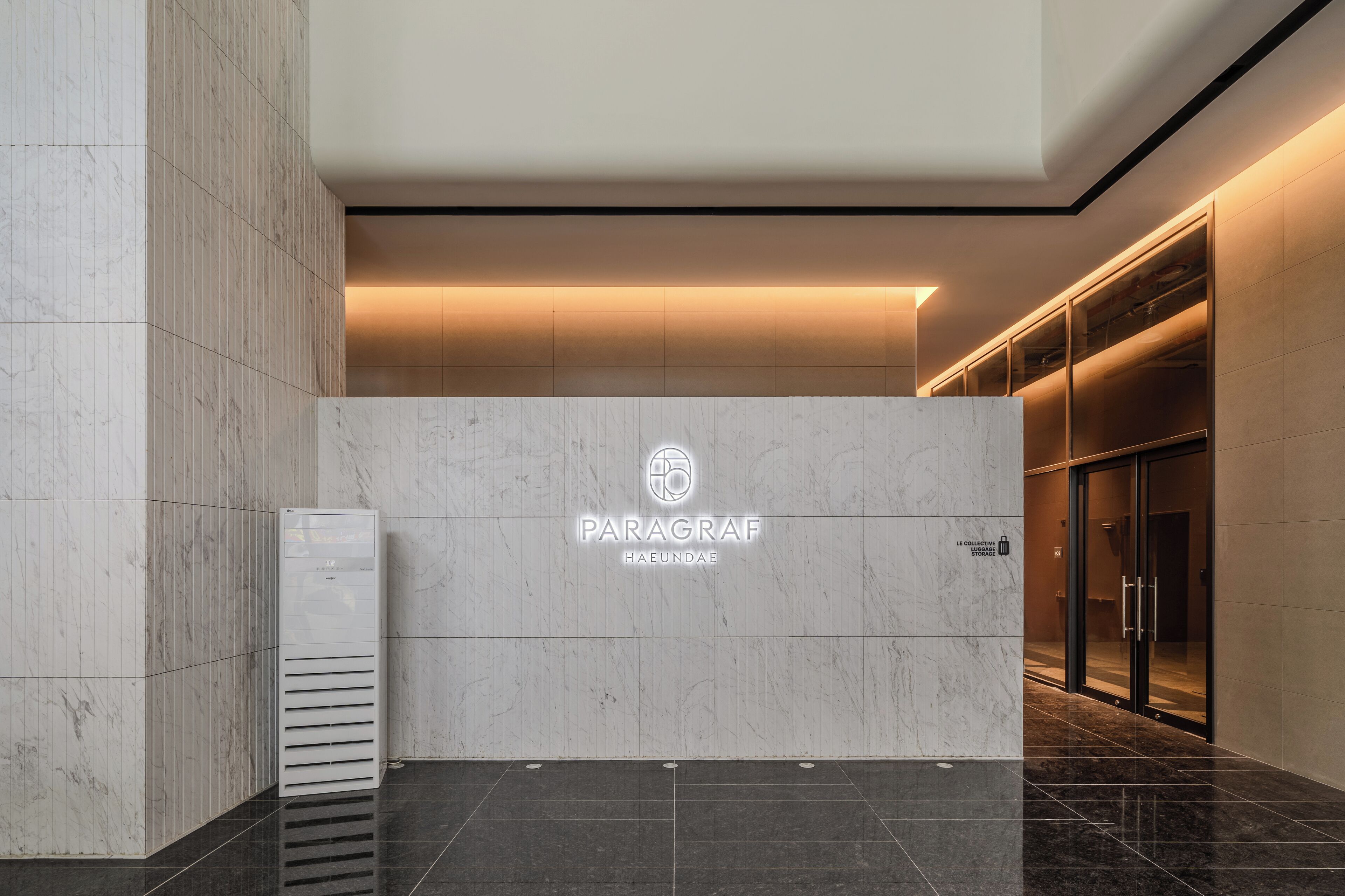 Interior moderno com parede de recepção em mármore, um logotipo e entrada por porta de vidro.