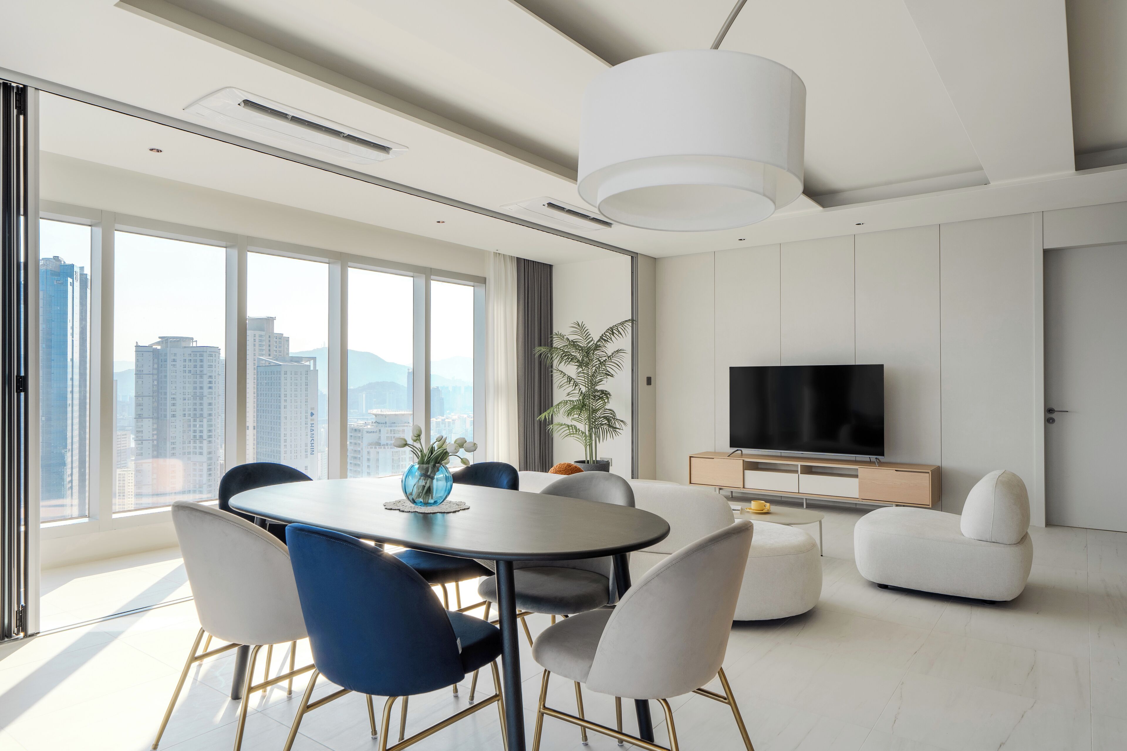 A modern living room with a dining area, large windows, and a flat-screen TV.