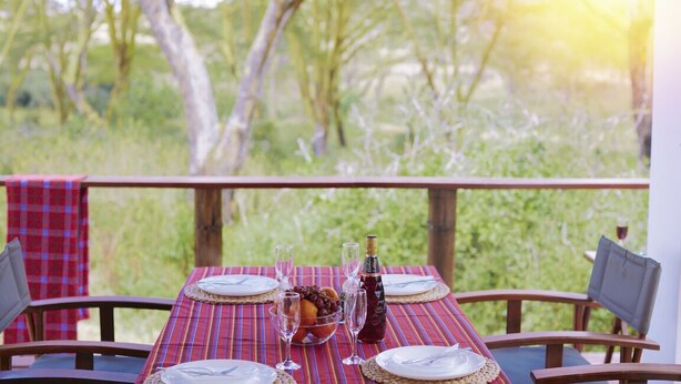 A table set outdoors with a view of greenery, a bottle, and a bowl of fruit. - Enjoy the Silence Apartments by YourHost (Naivasha)