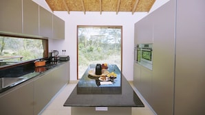 A modern kitchen with a central island, built-in appliances, and a large window offering a view of greenery. - Enjoy the Silence Apartments by YourHost (Naivasha)