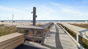 Una passerella in legno che conduce a una spiaggia con una torretta di salvataggio e una panchina.