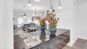 Una cucina moderna con un'isola grande, illuminazione a sospensione e vista sull'area pranzo.