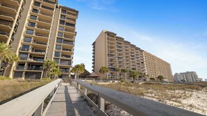 Un hotel sulla spiaggia con numerosi balconi, una passerella in legno e palme.