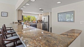 A modern kitchen with a granite countertop, stainless steel appliances, and a view of trees through the window. - Kokomo on Coco Plum at the Bonefish Yacht Club with 2 Boat Slips, Pool, Tennis/Pickle Ball Court, and Kayaks (Marathon)