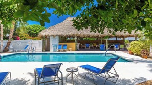A pool area with lounge chairs, a thatched-roof structure, and a sign indicating no diving.