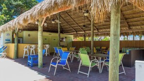 An outdoor dining area with thatched roofs, wooden pillars, and colorful chairs.
