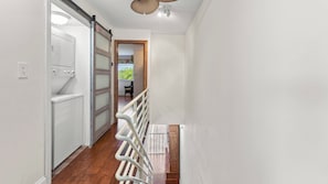 Un pasillo con lavadora, una puerta corredera y vista a otra habitación.