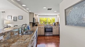 Una cocina moderna con encimeras de granito, electrodomésticos de acero inoxidable y un ventanal con vistas a árboles.