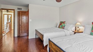 Una habitación con dos camas, una puerta de madera, una pared blanca y suelo de madera.