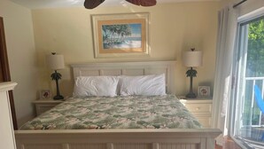A bedroom with a bed, two nightstands, a painting on the wall, and a window with curtains. - Kokomo on Coco Plum at the Bonefish Yacht Club with One Boat Slip, Pool, and a Tennis/Pickle Ball Court (Marathon)