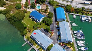 An aerial view of a marina with boats docked, a building with a blue roof, and a red star symbol on one of the buildings.