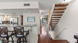 A modern kitchen with a bar area, wooden staircase, and a view of the outside.