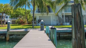 A wooden dock leading to a house with a garage, surrounded by palm trees and a clear blue sky. - Kokomo on Coco Plum at the Bonefish Yacht Club with 2 Boat Slips, Pool, Tennis/Pickle Ball Court, and Kayaks (Marathon)