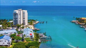 A coastal hotel with a prominent tower, marina, and lush greenery. - Kokomo on Coco Plum at the Bonefish Yacht Club with One Boat Slip, Pool, and a Tennis/Pickle Ball Court (Marathon)