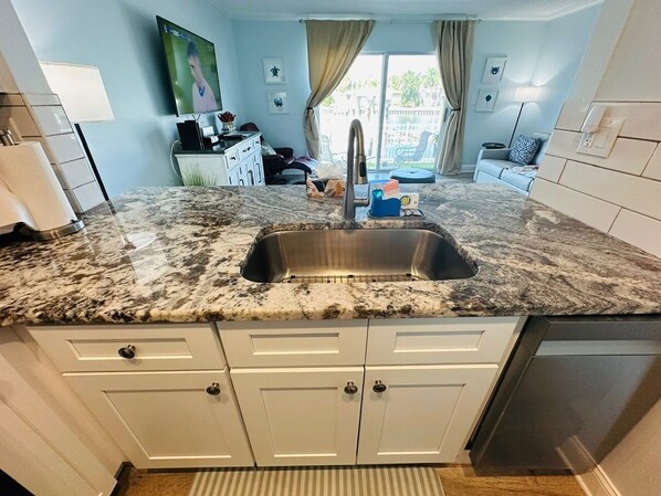 A kitchen with a granite countertop, stainless steel sink, white cabinets, and a dishwasher.