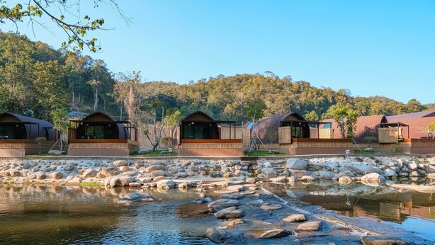 A row of cabins with a rocky stream in the foreground and a forested hill in the background. - Pang fan Rock & River Resort (Doi Saket)