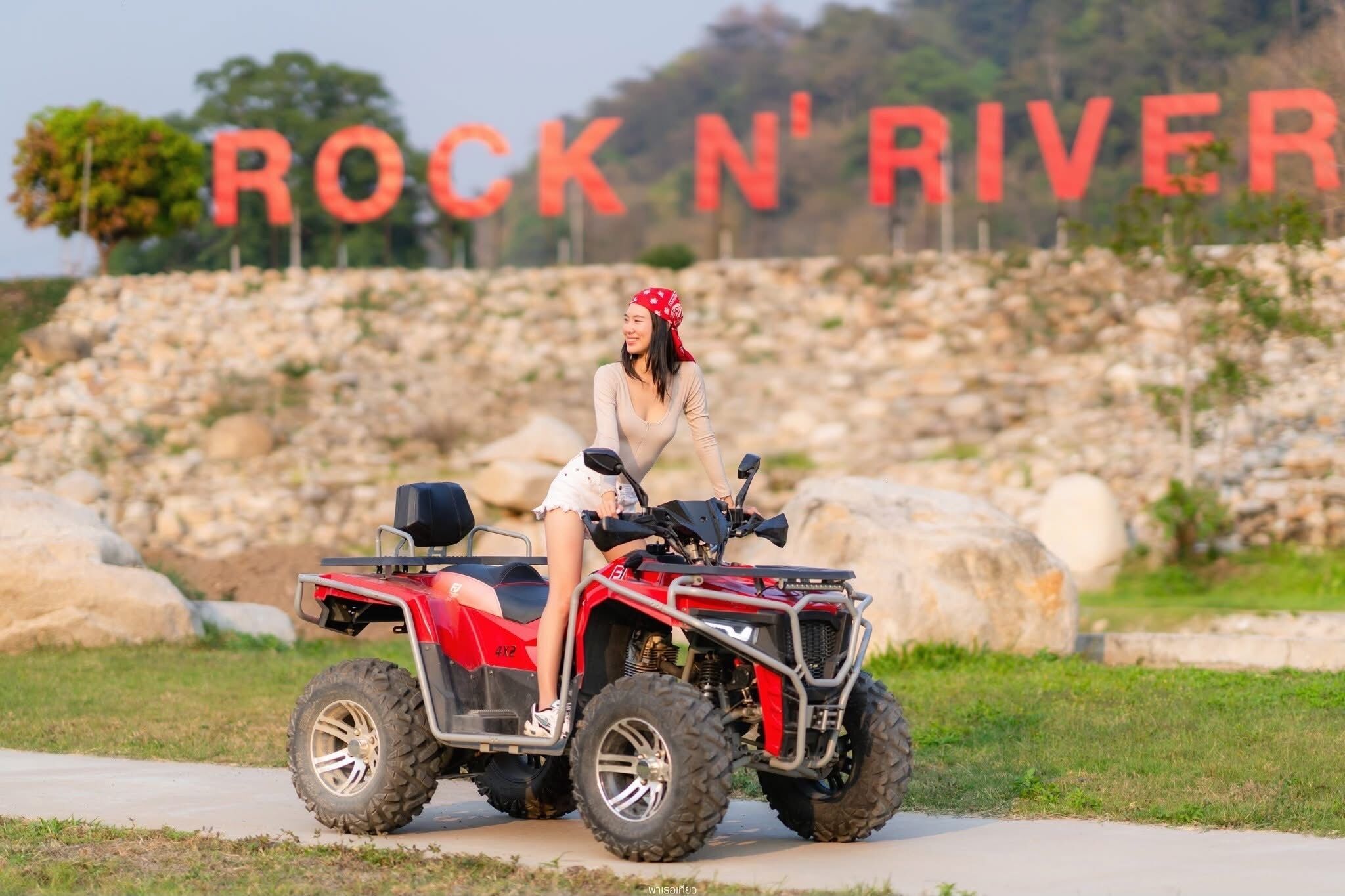 A person on a red ATV in front of a sign that reads "ROCK N' RIVER".