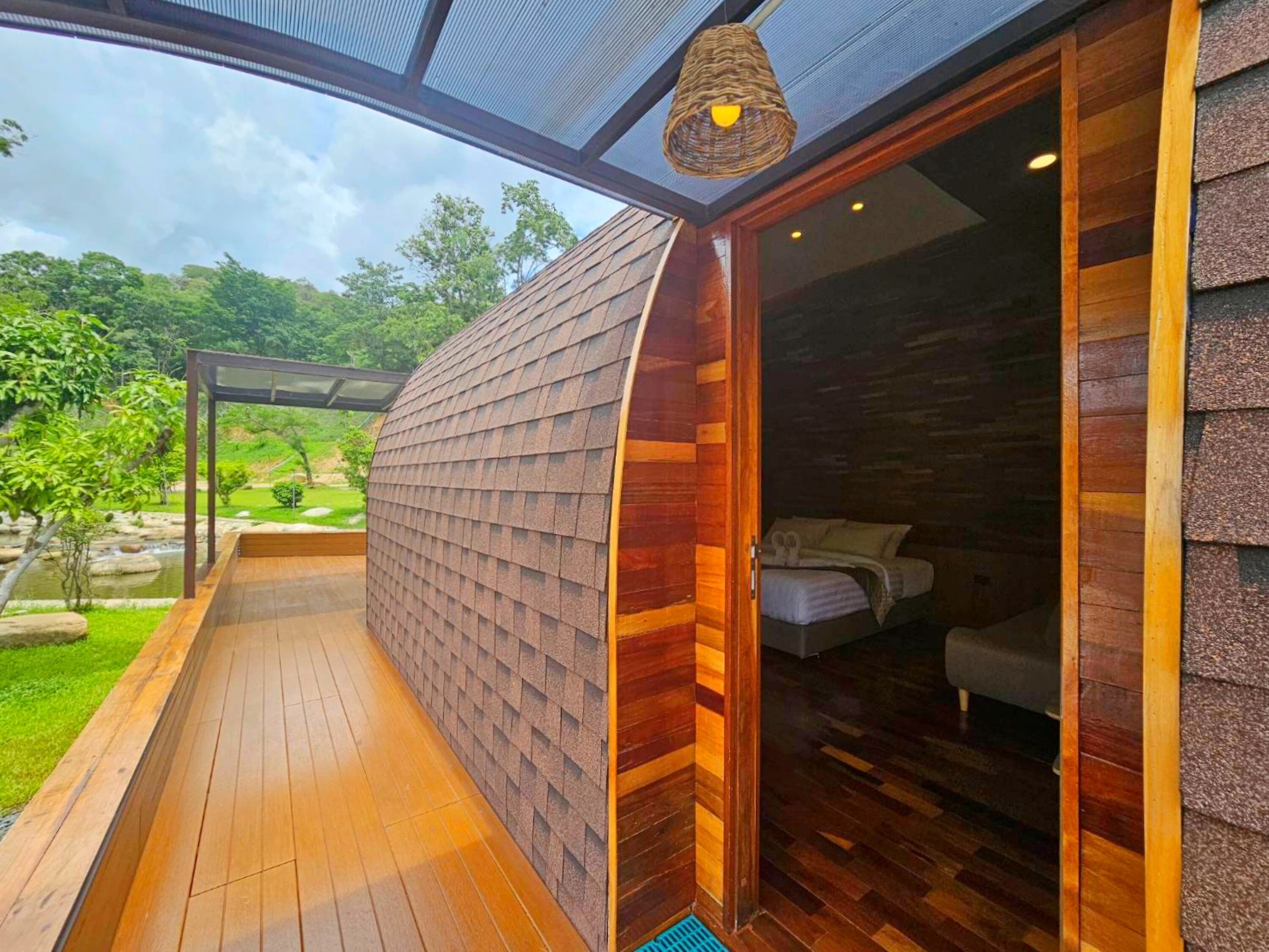 A modern building with a wooden exterior, a wooden deck, and a glass door leading to a bedroom with a bed and a nightstand.
