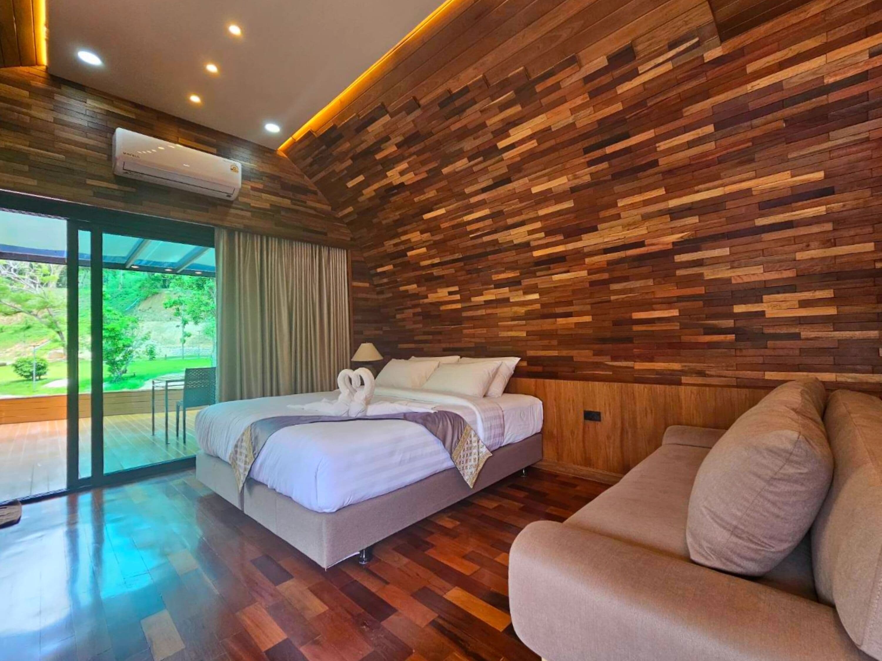 Un dormitorio moderno con pared de madera, una cama, un sofá y vistas al exterior.
