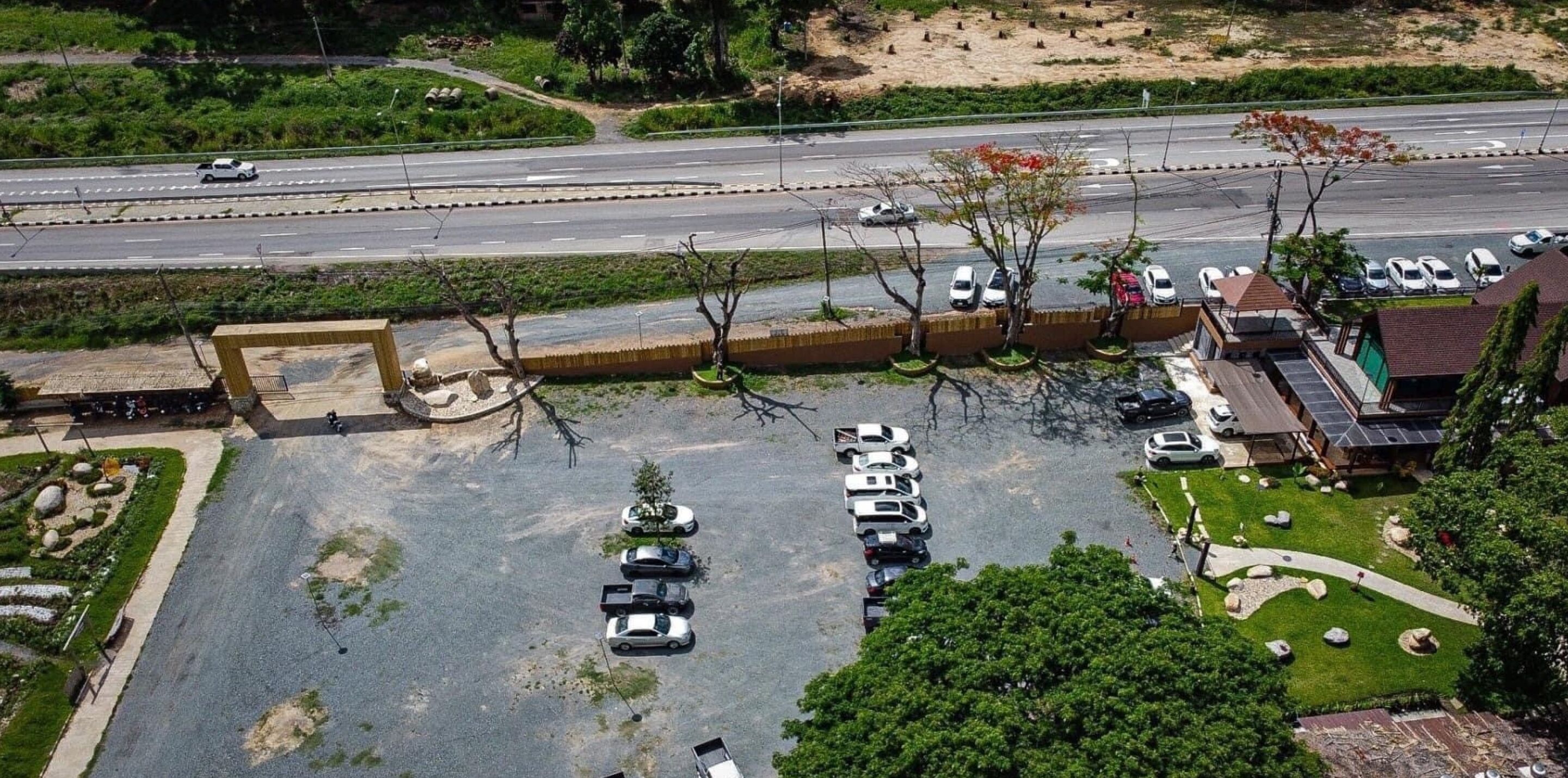 An aerial view of a parking lot with multiple cars, a small building, and a road in the background.