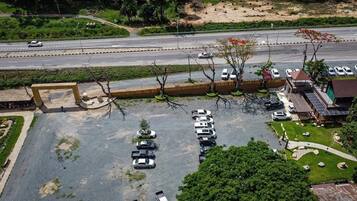 An aerial view of a parking lot with multiple cars, a small building, and a road in the background.