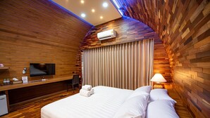 A modern hotel room with a wooden wall design, a flat-screen TV, a desk with a chair, a bed with white linens, and an air conditioning unit. - Pang fan Rock & River Resort (Doi Saket)