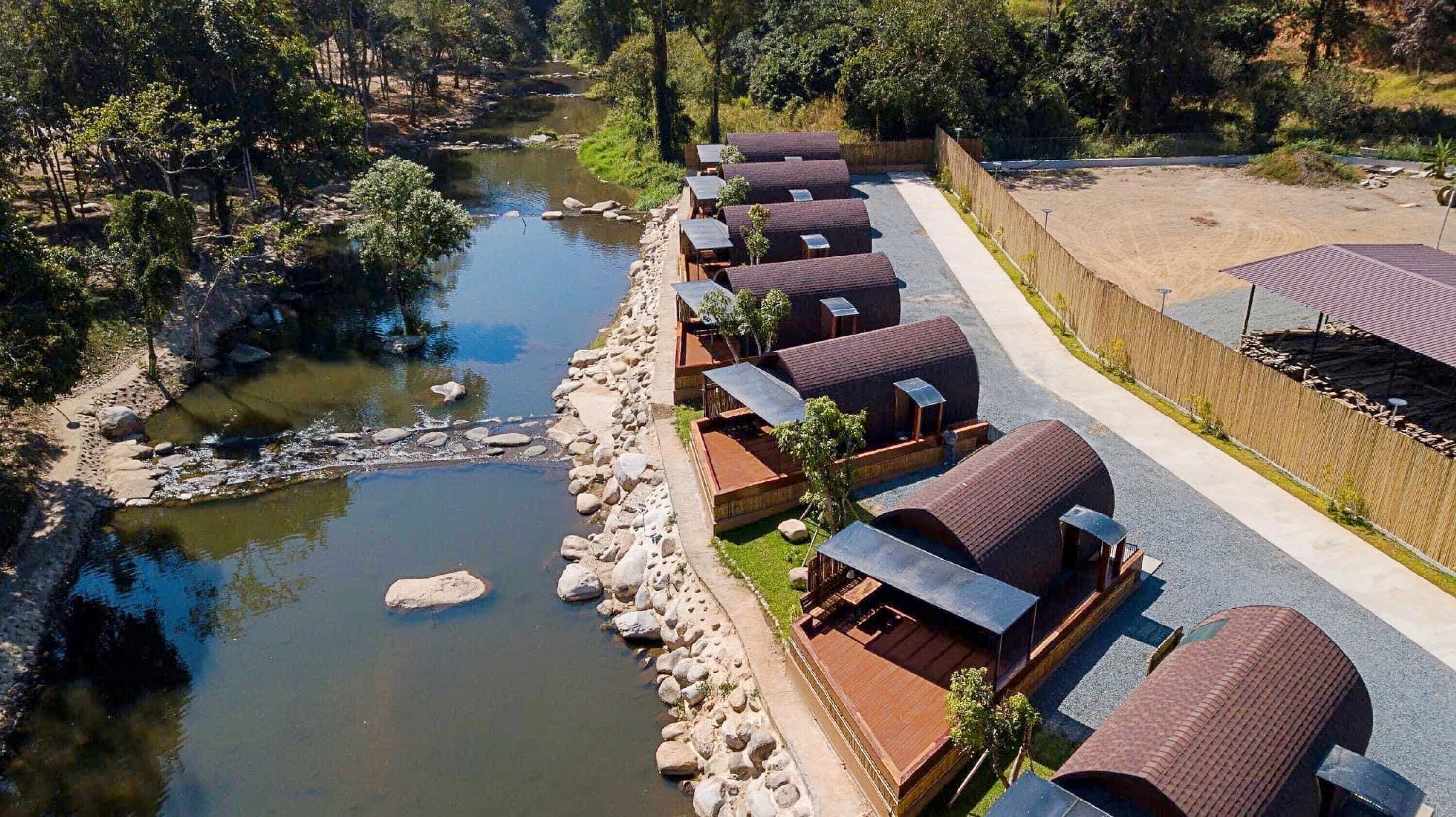 Una hilera de cabañas con un río y terreno rocoso al fondo.