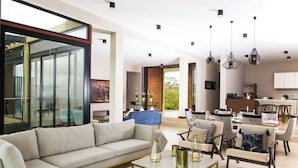 A modern living room with a sofa, coffee table, and dining area with chairs. - Champagne Ridge Villa by YourHost Kenya (Olooloitikosh)