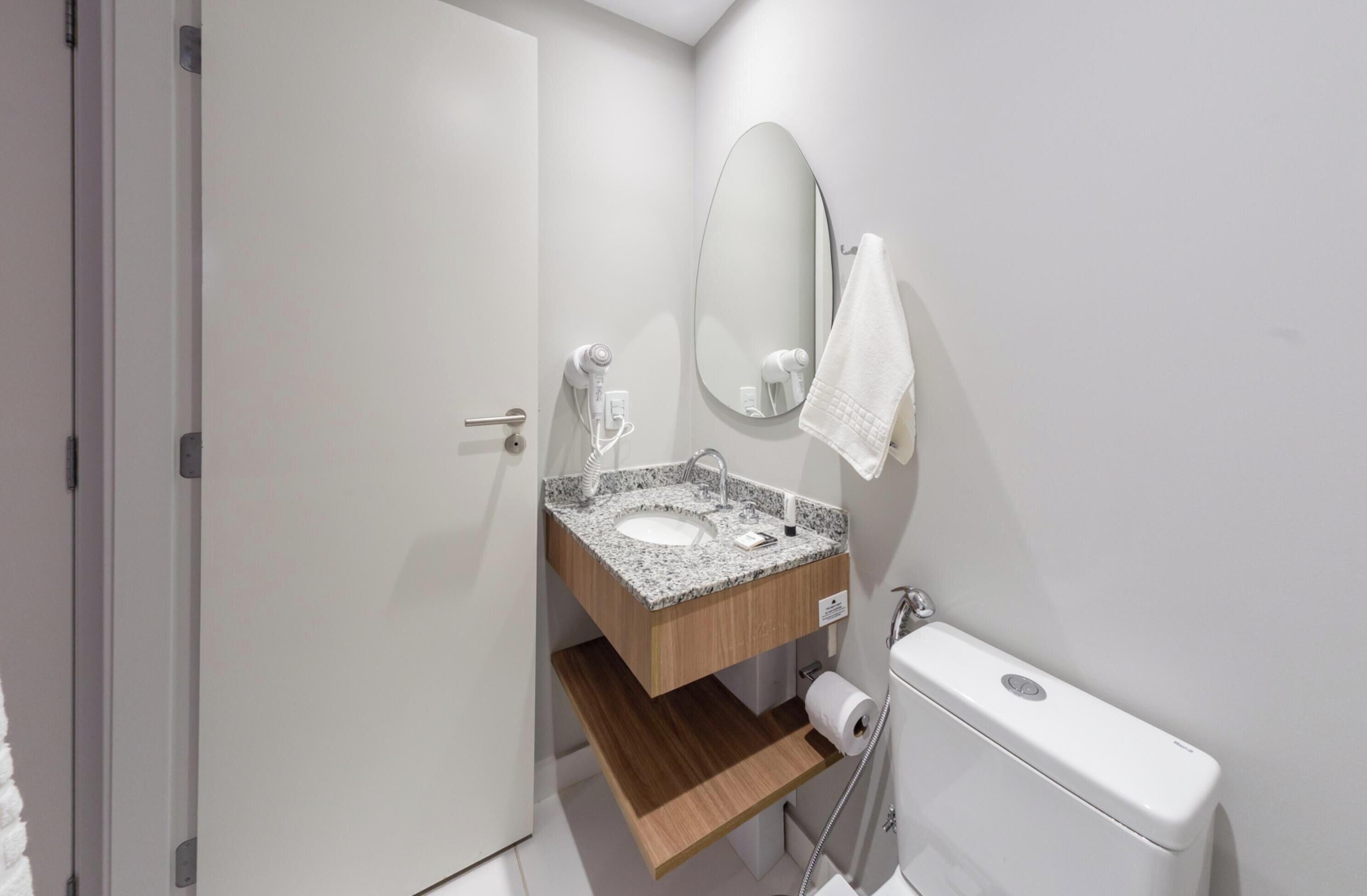 A modern bathroom with a granite countertop sink, a mirror, a towel hanging on the wall, and a toilet.