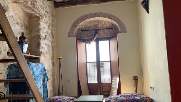 Una habitación acogedora con una escalera de madera, un cojín estampado, una mesita y un ventanal de arco decorativo.