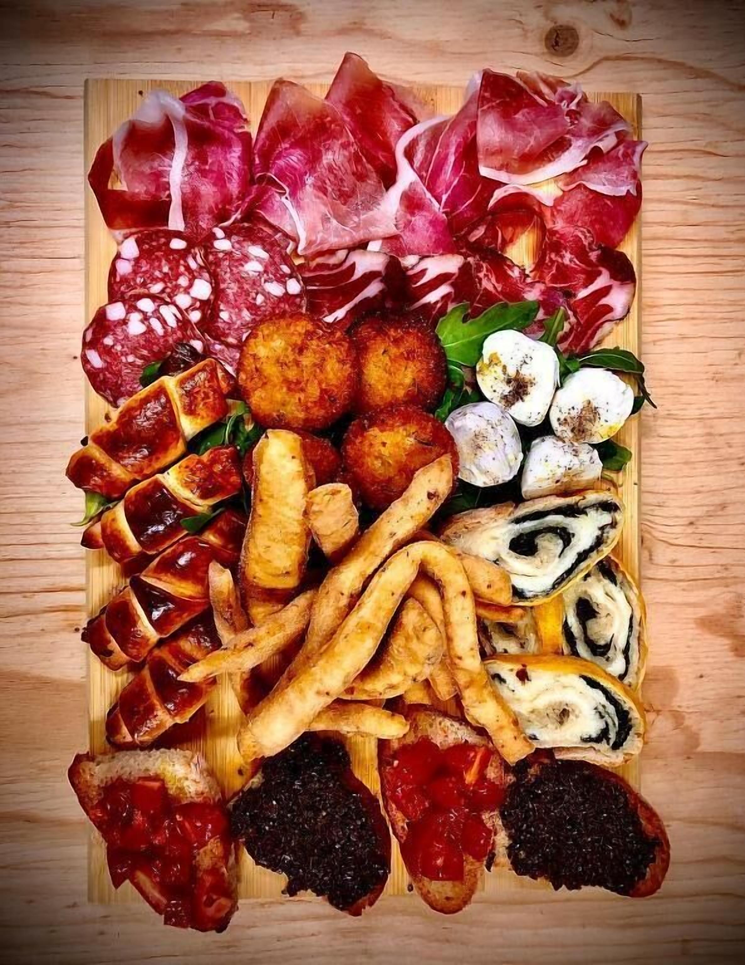 Une planche en bois sur laquelle sont disposés divers aliments, notamment de la charcuterie, du pain et des légumes.