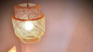 Een houten trap met een witte leuning, een geweven lamp en een klein tafeltje met een vaas.