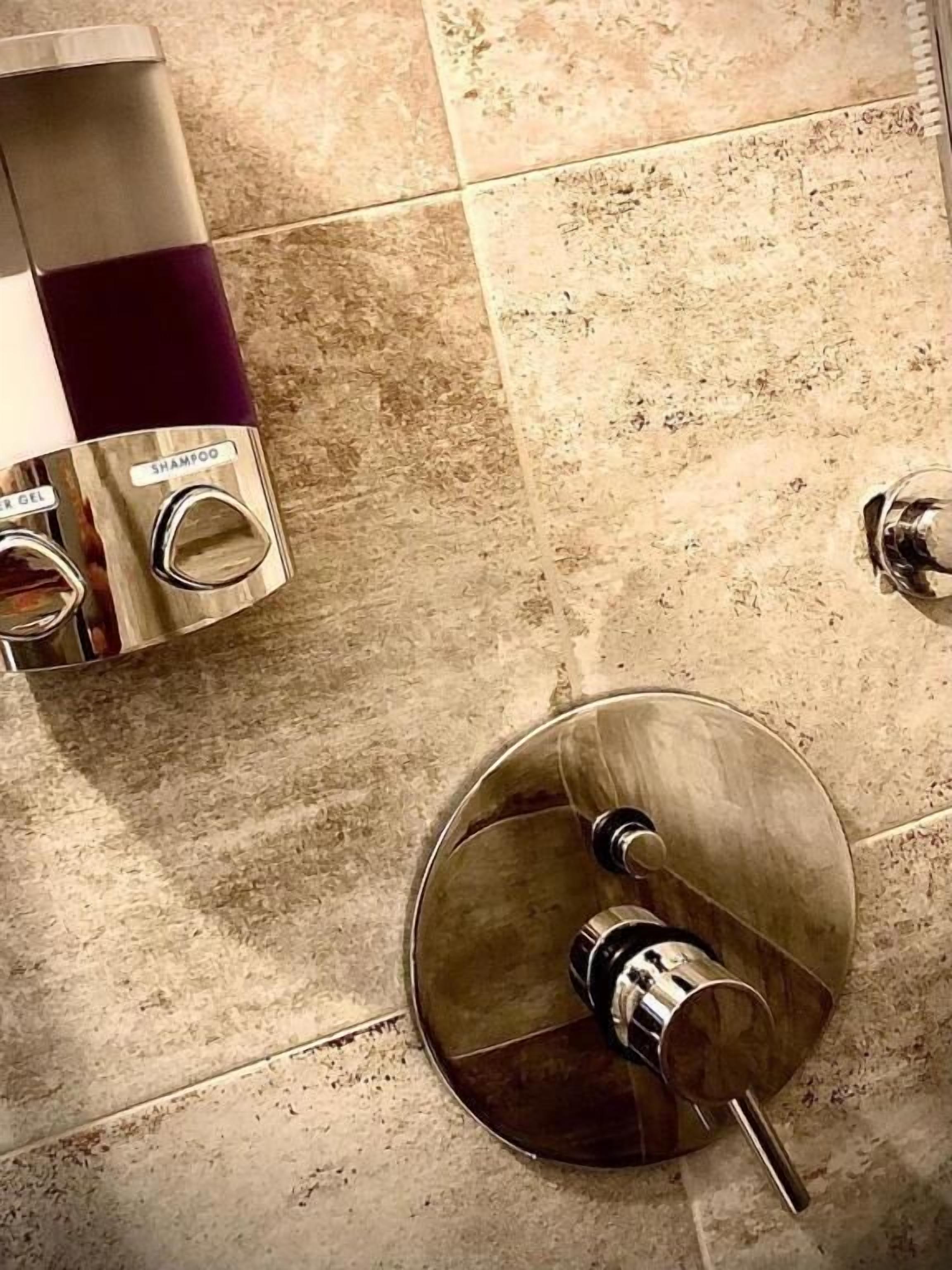 Een badkamer met een marmeren vloer, een spiegel en een fles shampoo op een plank.