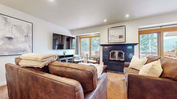 Una sala de estar moderna con sofás de cuero, una chimenea y ventanas amplias que ofrecen vistas al exterior.
