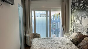 Habitación de hotel con una cama grande, una silla, un balcón con vistas al mar y un mural temático tropical.