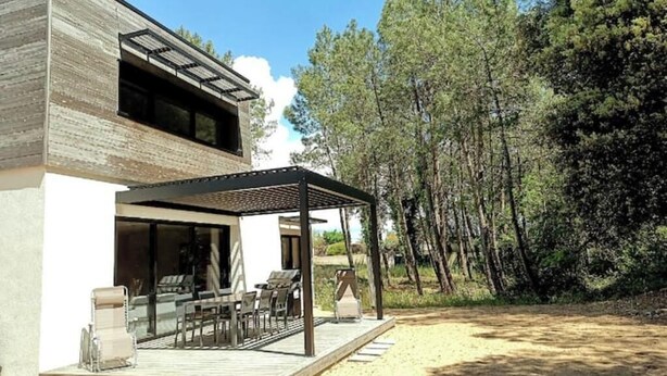 Una casa moderna con una terrazza in legno, arredi da esterno e un pergolato.