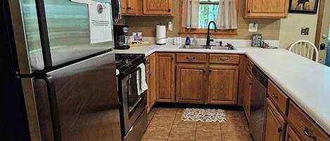 A kitchen with wooden cabinets, a stainless steel refrigerator, a stove, and a sink.