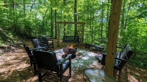 Ein bewaldeter Campingplatz mit Feuerstelle, Holzbänken und Picknicktischen.