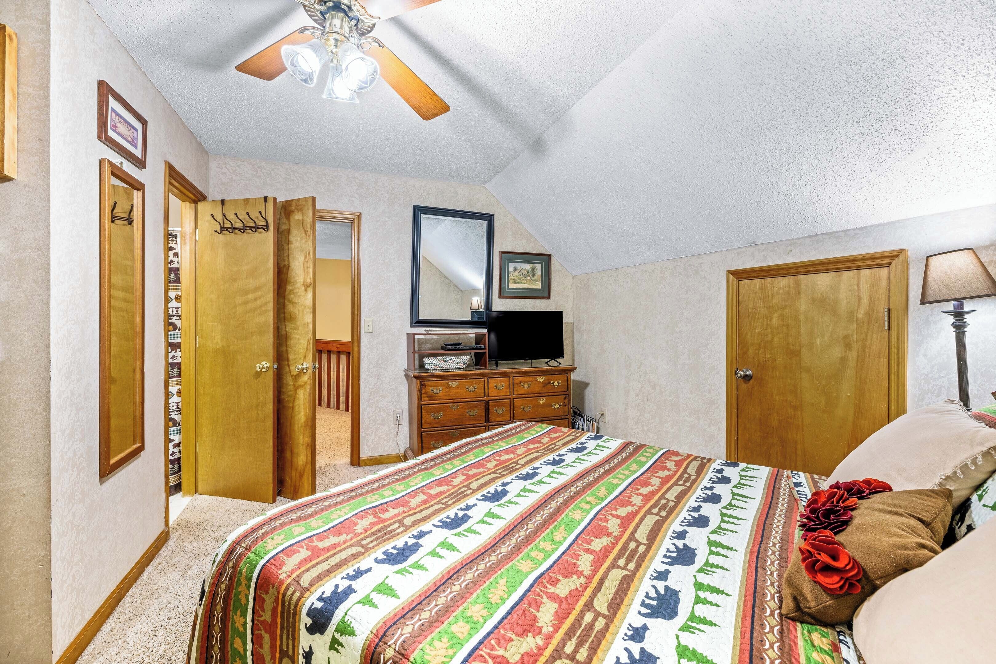Un dormitorio con cama, cómoda, televisor y ventilador de techo.