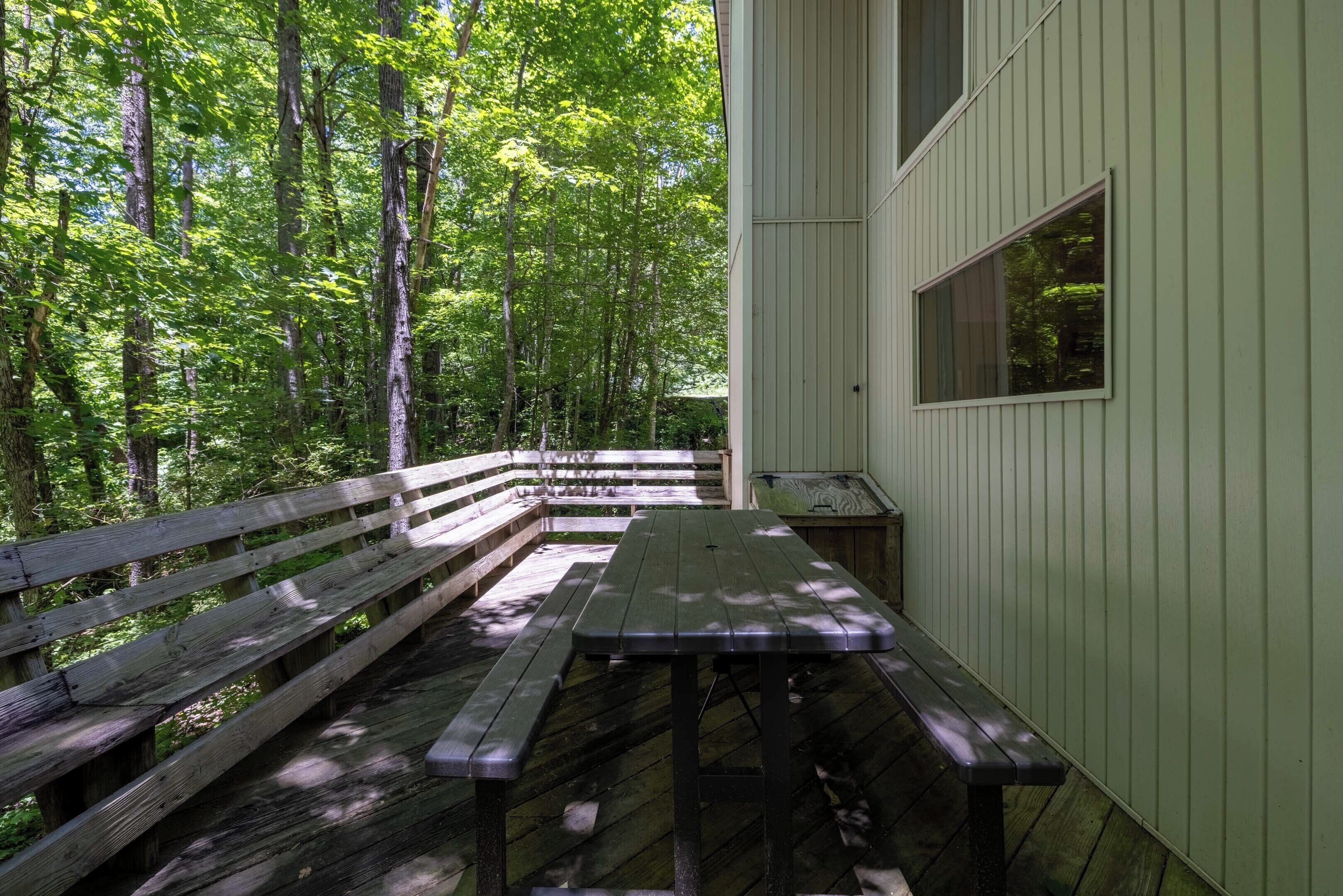 A picnic table in a forested area with a wooden bench and a small table nearby.