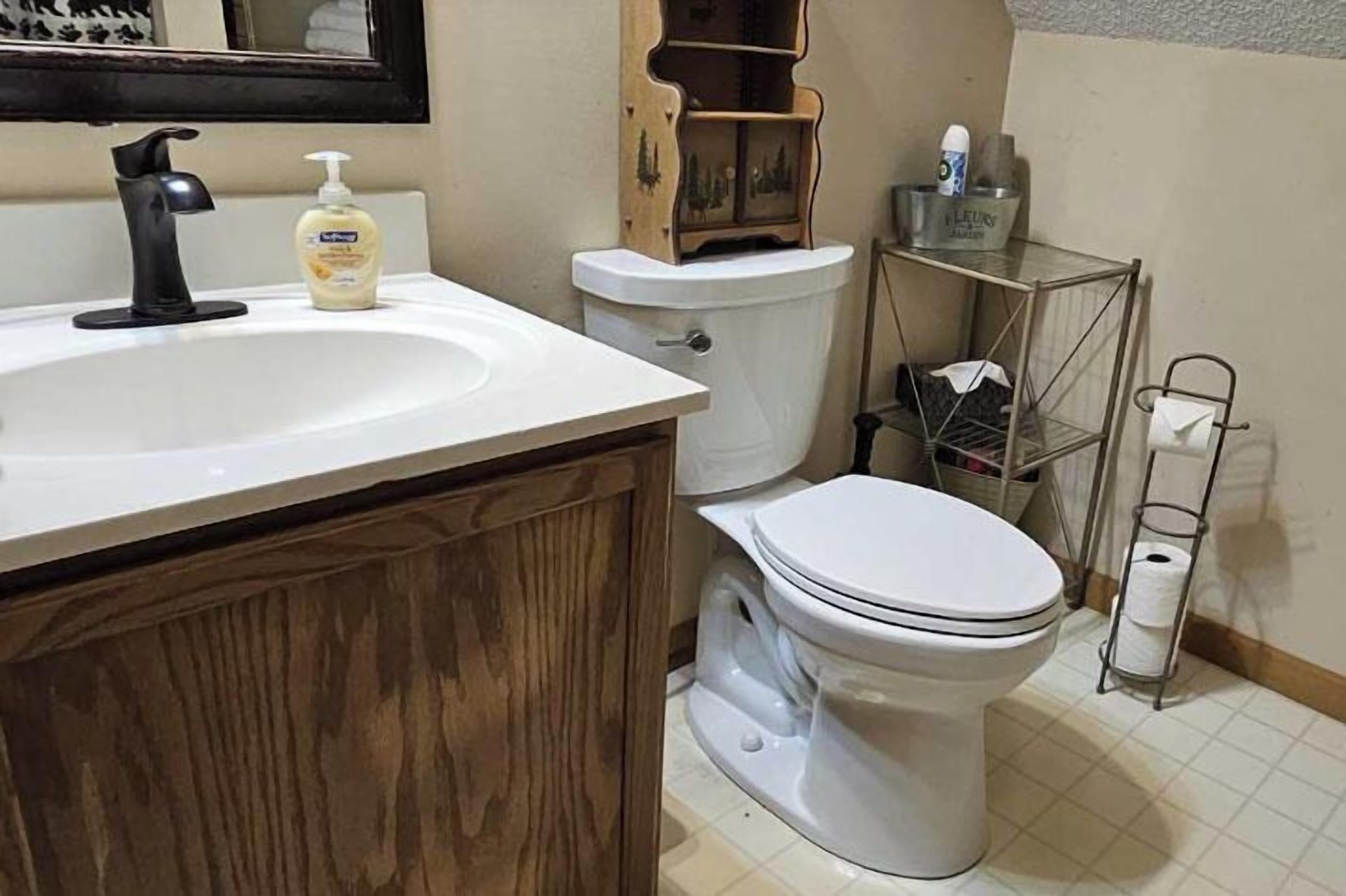 A bathroom with a white sink, black faucet, and a toilet. There is a wooden cabinet under the sink and a shelf with toiletries.