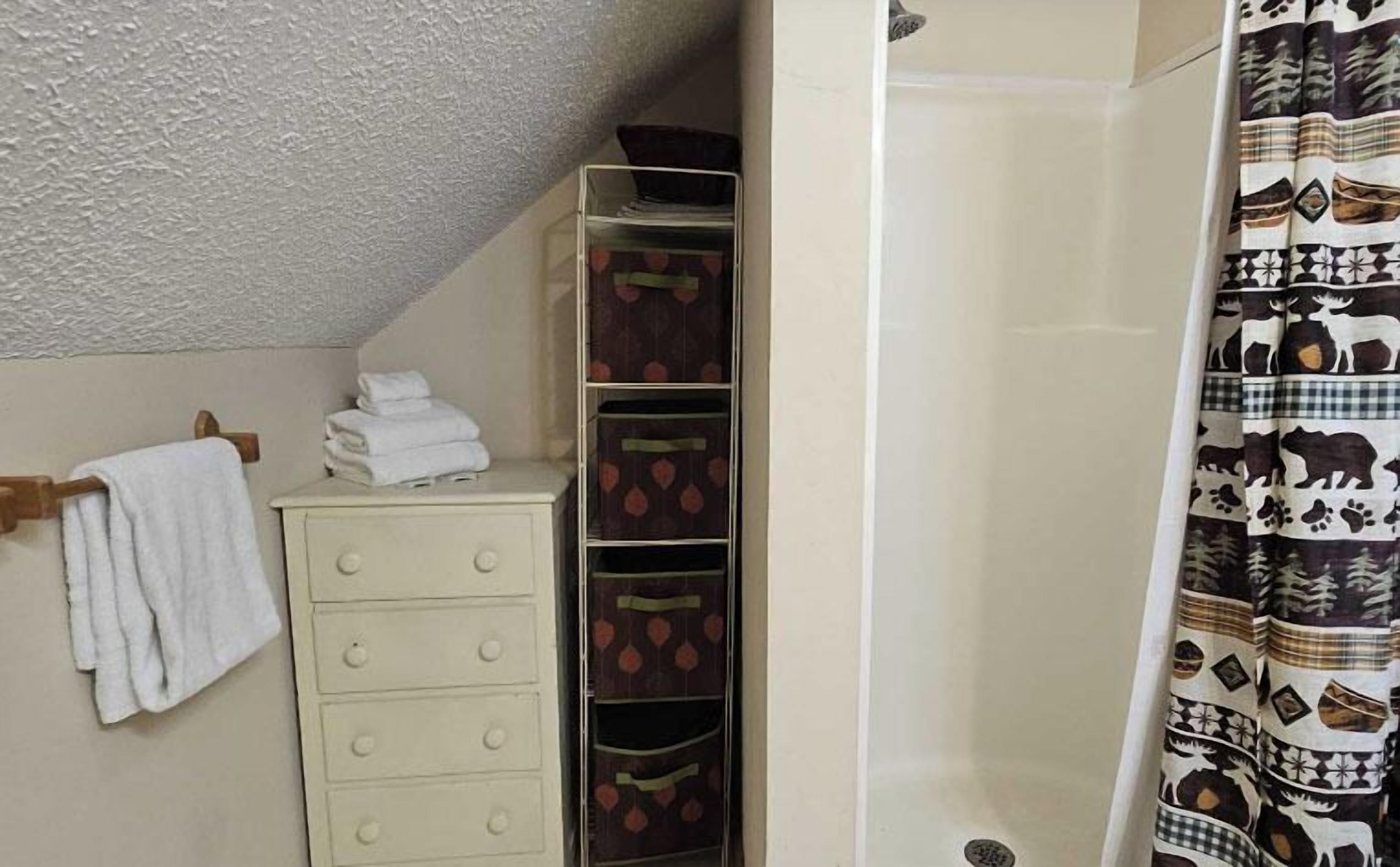 A bathroom with a white cabinet, a towel rack, a shower curtain with animal prints, and a textured ceiling.