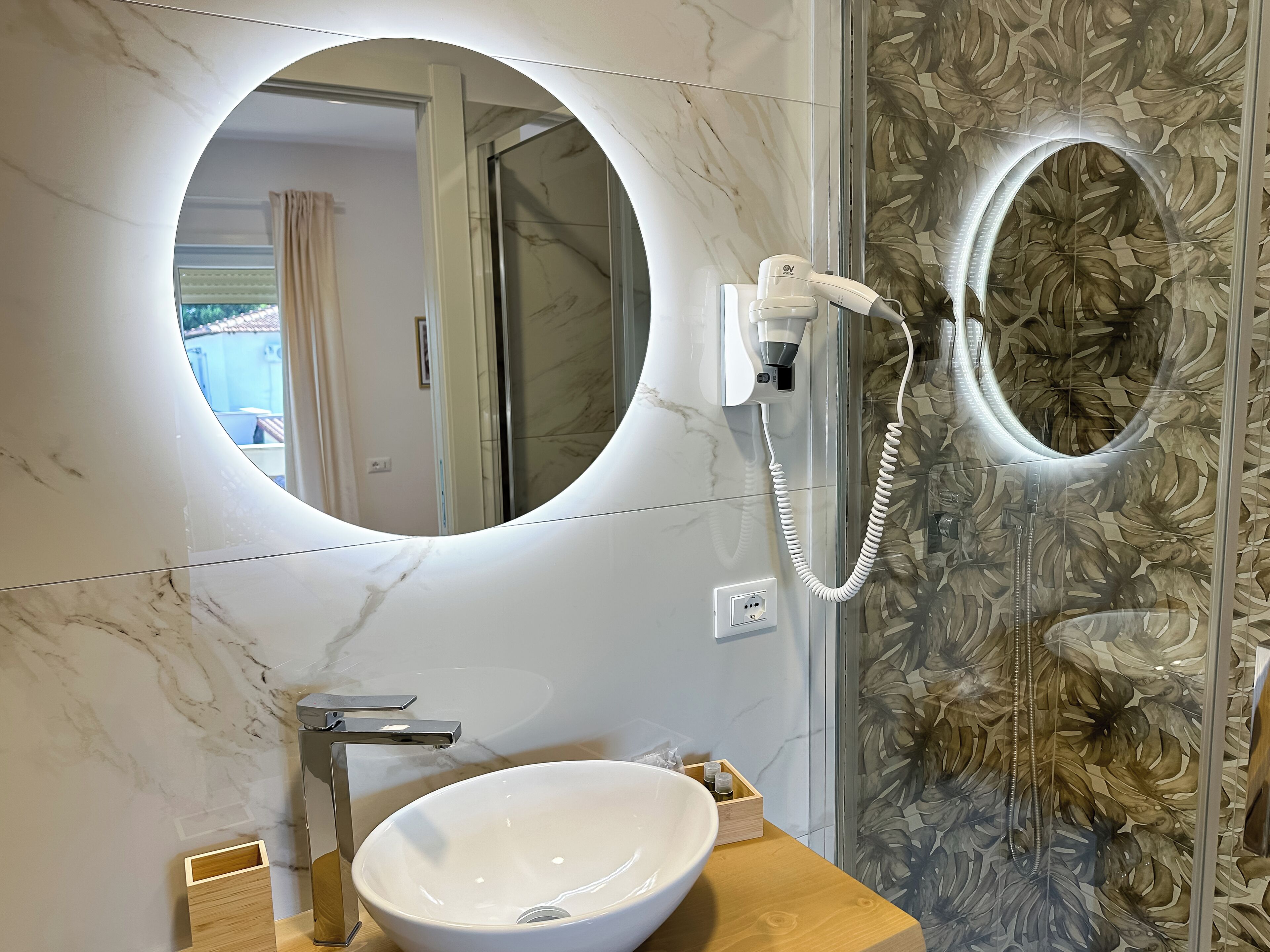 Une salle de bain avec un miroir rond, un lavabo blanc et un espace douche.